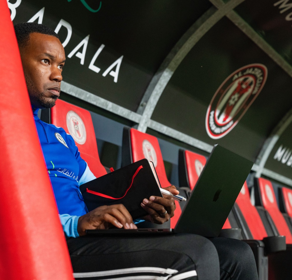 Dazell Young in the Al Jazira dugout with a laptop and notebook